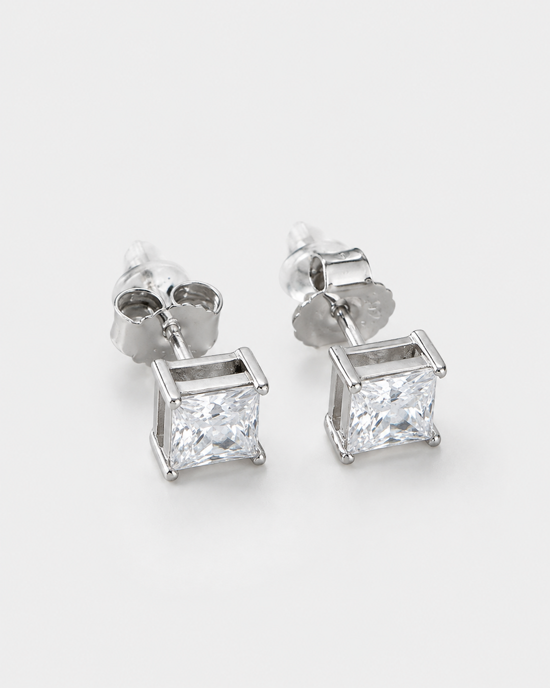 A pair of silver stud earrings featuring square princess-cut clear gemstones in a four-prong setting, shown on a clean white background.
