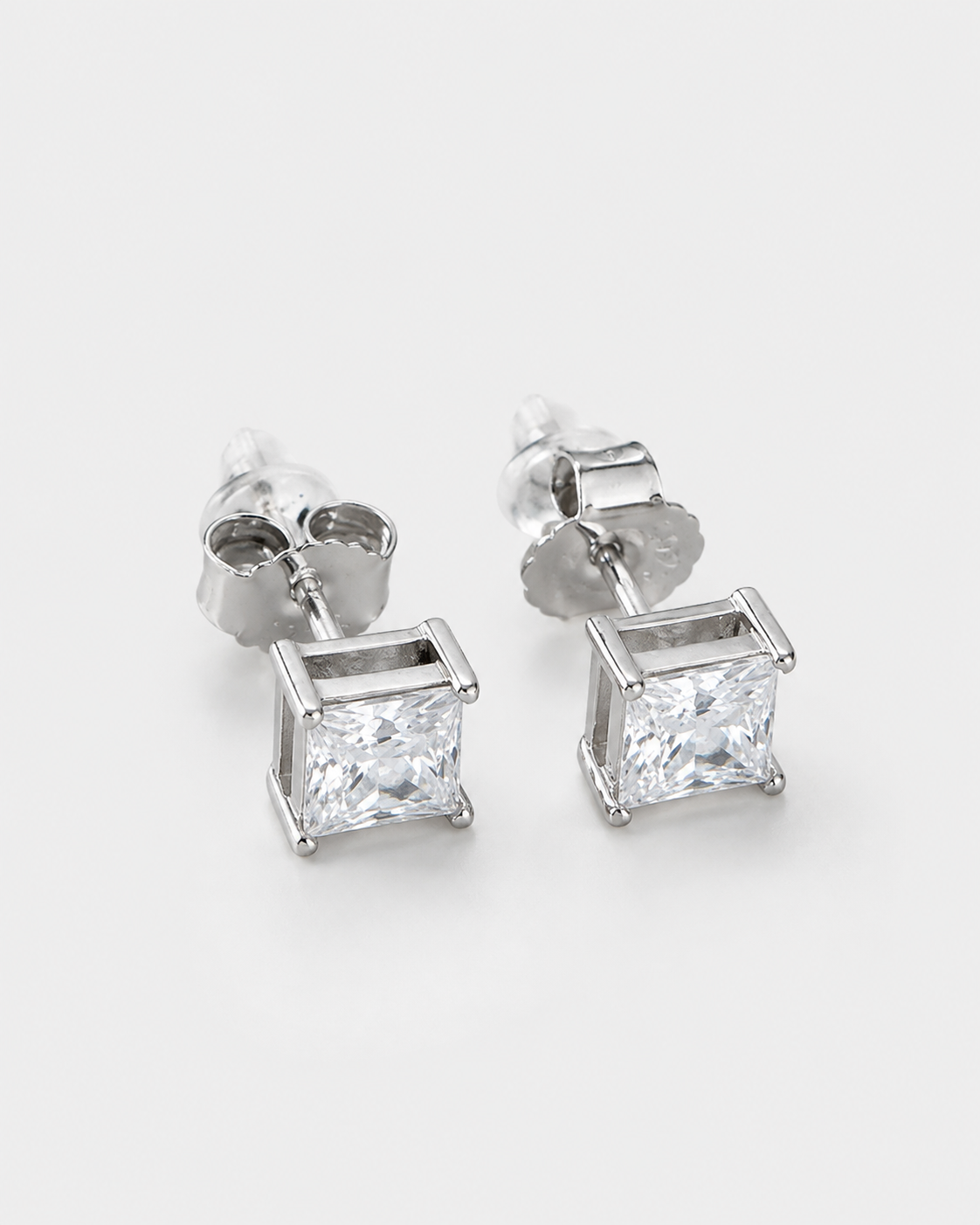 A pair of silver stud earrings featuring square princess-cut clear gemstones in a four-prong setting, shown on a clean white background.